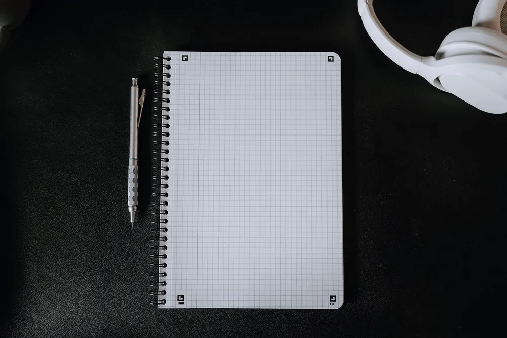 Carnet à spirale, stylo à bille et casque audio blanc sur un bureau noir